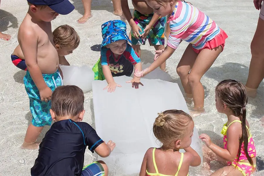 Children sit in pool around ice cube