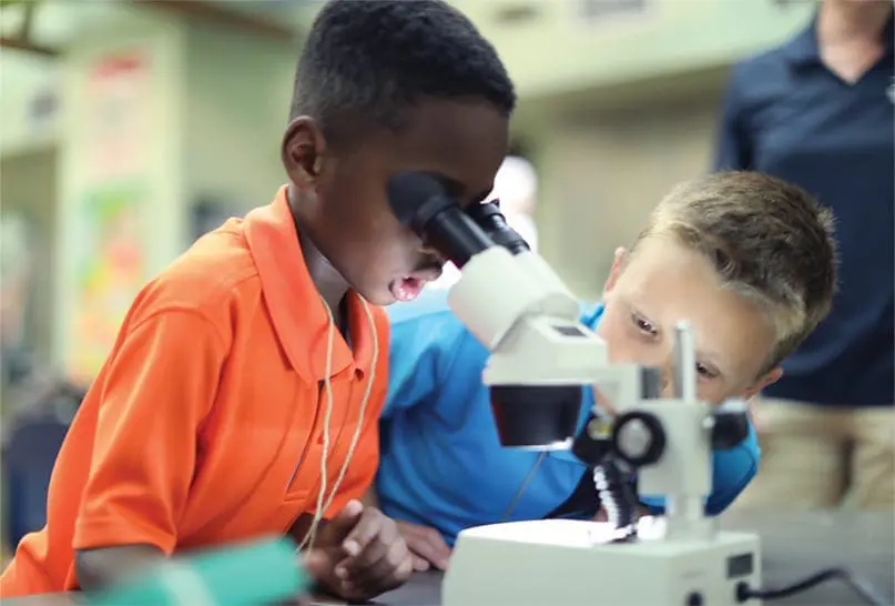 Two boys peer through a microscope.