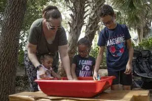 A family explores a container of dirt and plastic animals