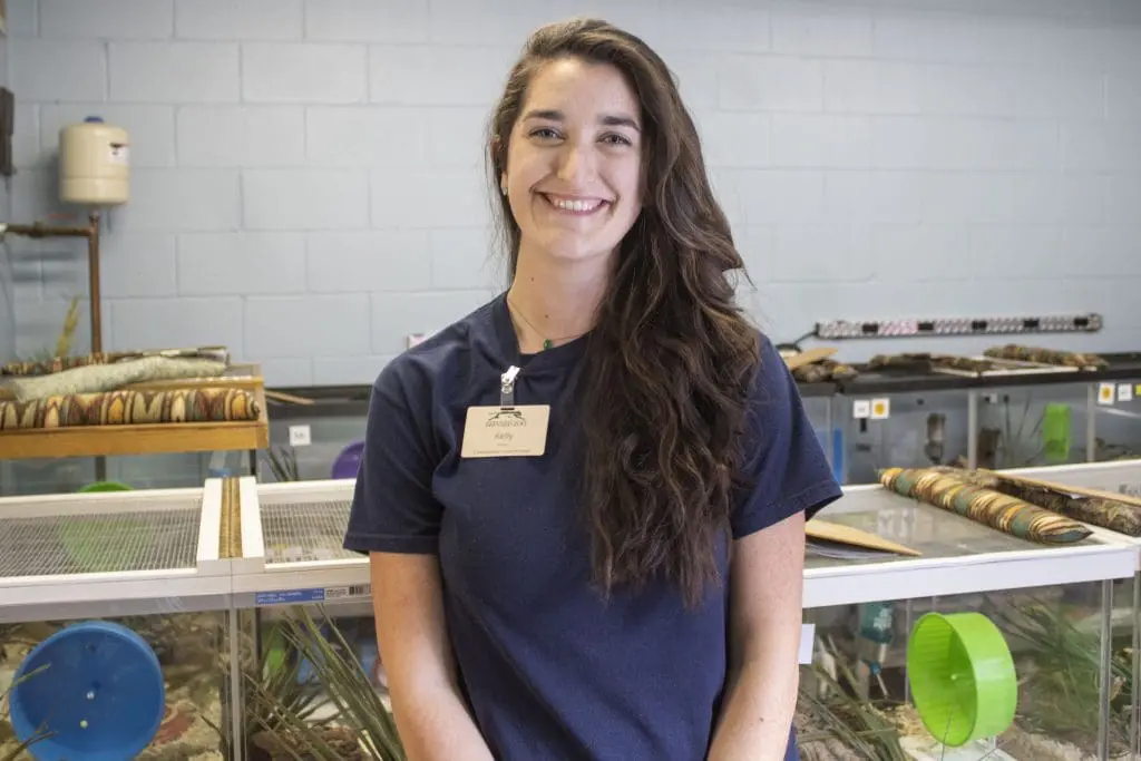 A woman stands surrounded by aquarium tanks.