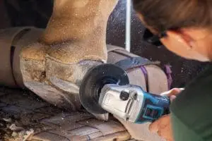 A keeper buffs Rafiki the giraffe's foot using power tools.