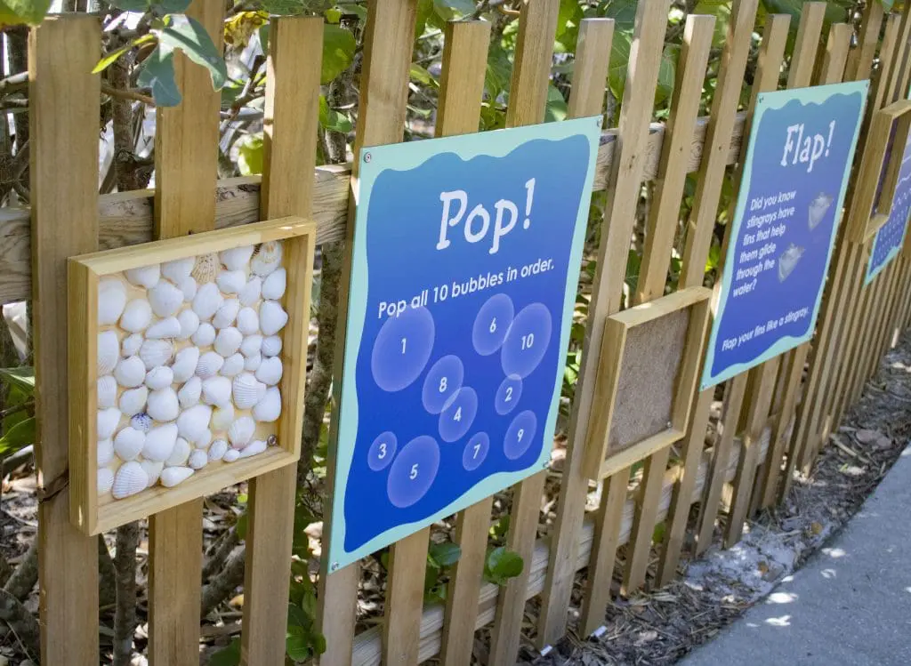 Signs and art displays on a fence encouraging viewers to move and touch.