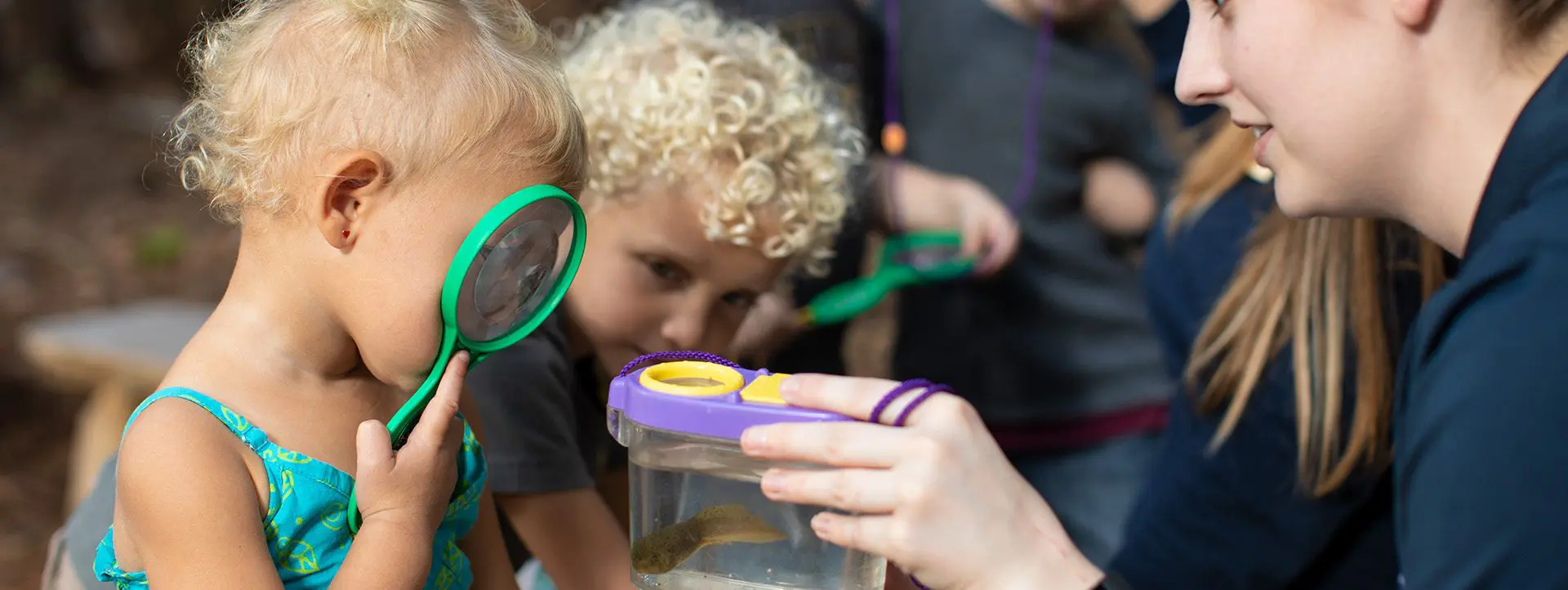 girl looking at a wiggly wonder in a container through a magnifying glass held up to her eye