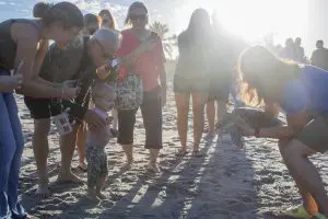 A crowd looks at a woman holding a sea turtle on a beach.