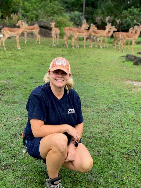 A woman standing with impala in the background. 