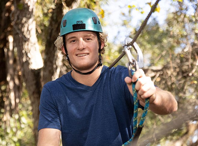 Smiling guy on a zipline at Brevard Zoo's Treetop Trek experience.