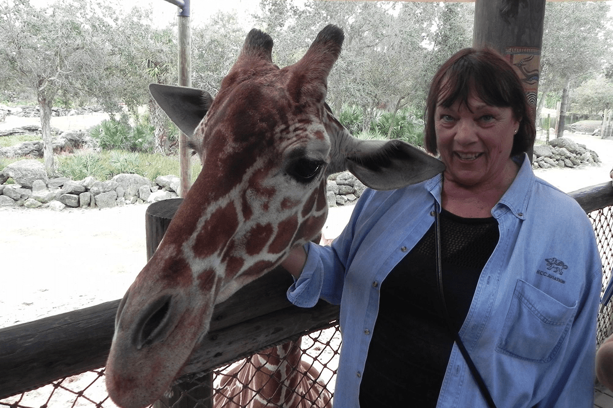 a woman smiling next to Rafiki the giraffe.