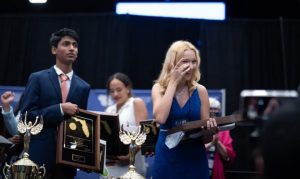 A young man stands alongside a young girl while they both hold trophies.