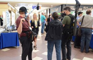 A camera crew surrounding a young girl while filming her at a science fair.