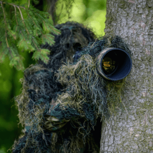 A photographer wears a ghillie suit in the woods.